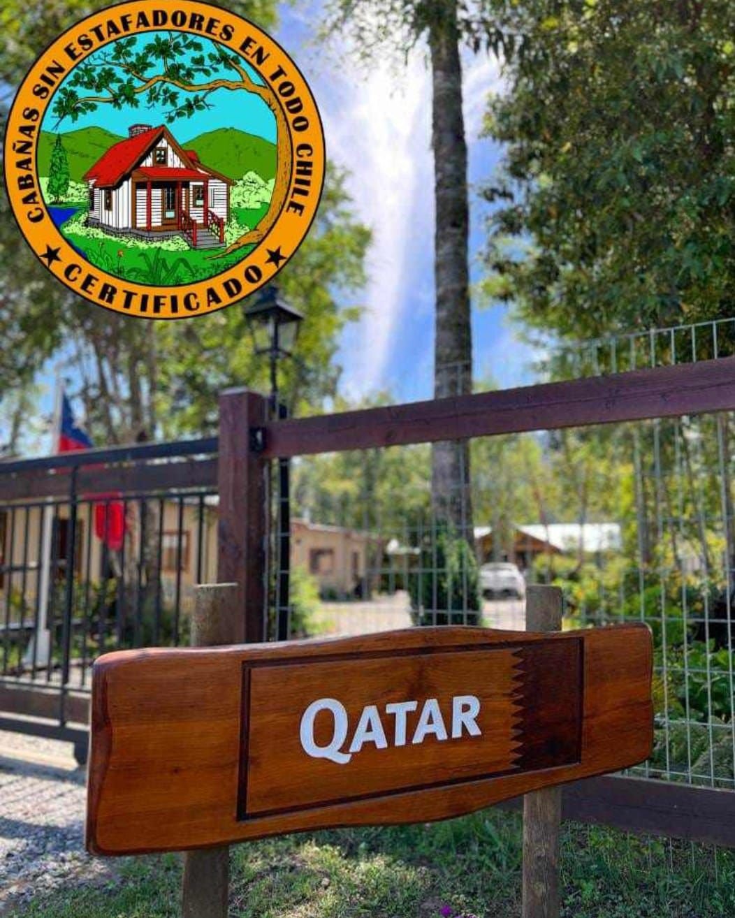 Letrero de madera “Qatar” en el portón de entrada, con jardín al fondo